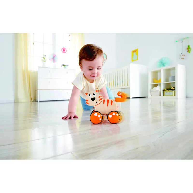 Ein Baby krabbelt auf Holzboden und greift in einem hellen Raum nach einem orangefarbenen Tiger-Spielzeug auf Rädern. Ein Baby krabbelt auf Holzboden und greift in einem hellen Raum nach einem orangefarbenen Tiger-Spielzeug auf Rädern.