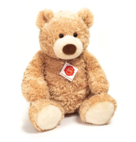 Ein hellbrauner Plüsch-Teddybär mit weißer Schnauze und Pfoten sitzt aufrecht, ein Schild an der Brust.