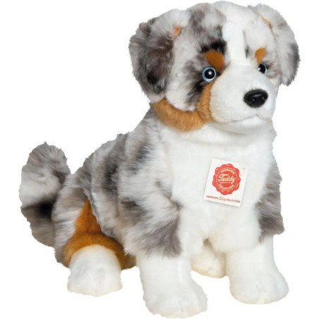 Plüschhund mit grau-weiß-braun-schwarzem Fell sitzt aufrecht, Brust mit einem Etikett versehen.