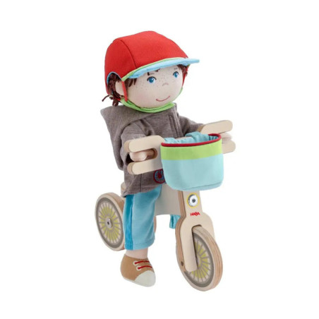 Stoffpuppe mit rotem Helm fährt auf einem Holzfahrrad mit blauem Korb vor weißem Hintergrund. Stoffpuppe mit rotem Helm fährt auf einem Holzfahrrad mit blauem Korb vor weißem Hintergrund.