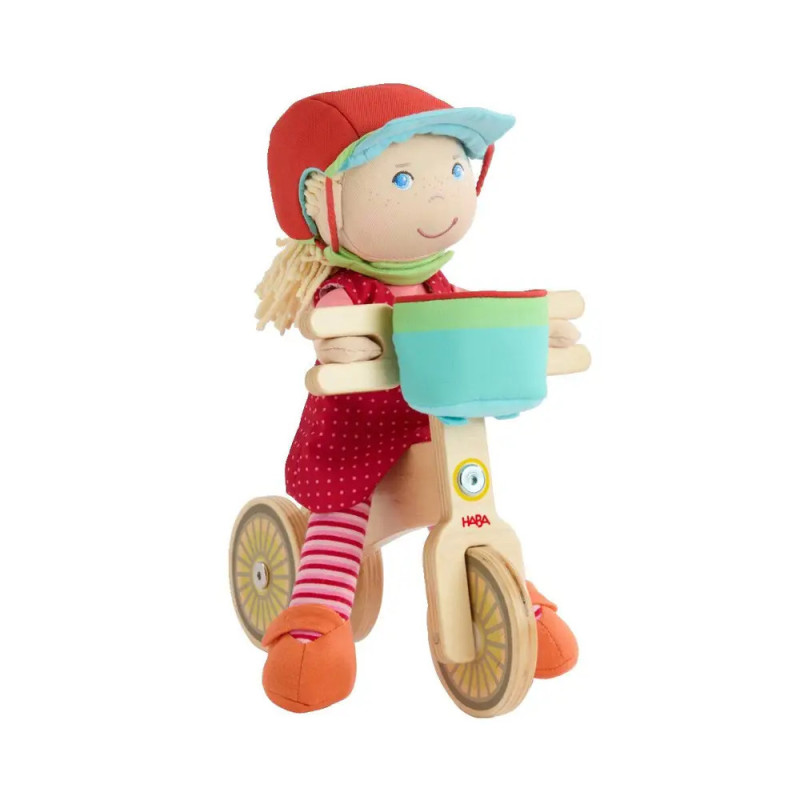 Plüschpuppe mit rotem Helm fährt auf Holz-Dreirad mit blauem Korb, vor weißem Hintergrund.