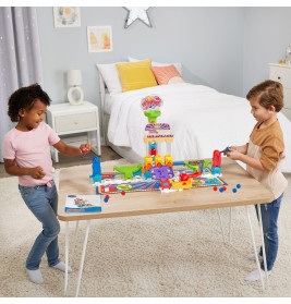 Zwei Kinder spielen ein buntes Brettspiel am Tisch in einem gemütlich, ordentlich eingerichteten Schlafzimmer.