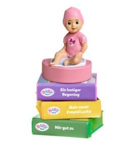 Eine kleine Puppe in Pink sitzt auf bunten, gestapelten Boxen mit deutscher Beschriftung an den Seiten.