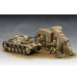 Modellpanzer und zwei Spielfiguren stehen neben einer beschädigten, bemalten Mauer in einer Wüstenszene.