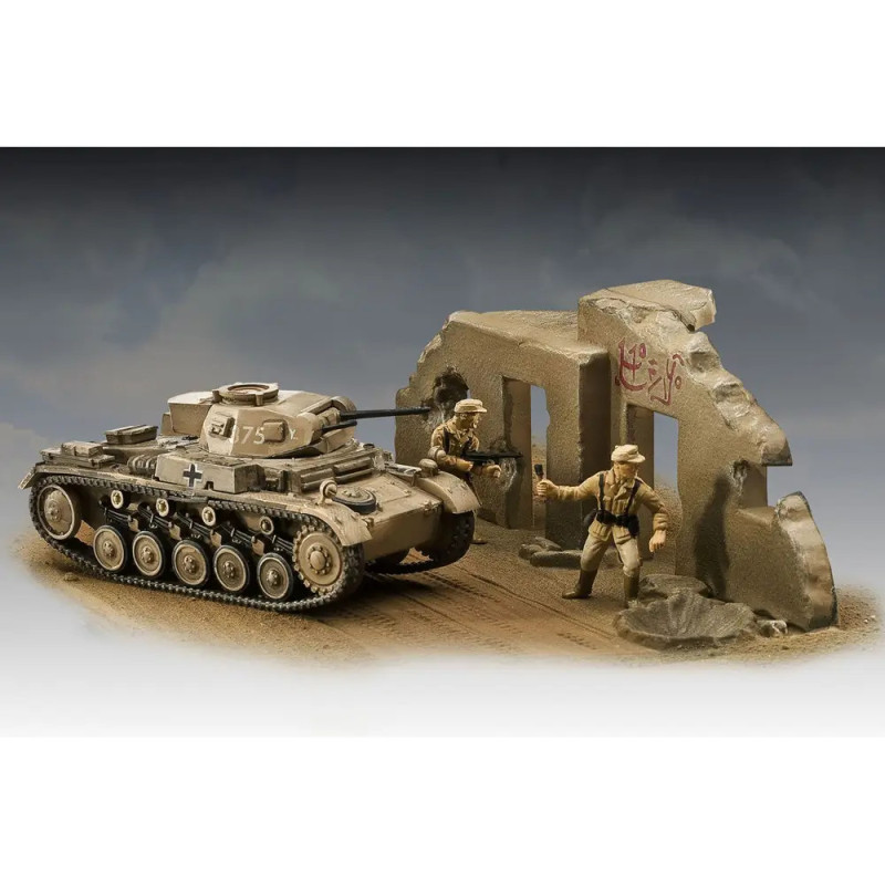 Modellpanzer und zwei Spielfiguren stehen neben einer beschädigten, bemalten Mauer in einer Wüstenszene. Modellpanzer und zwei Spielfiguren stehen neben einer beschädigten, bemalten Mauer in einer Wüstenszene.