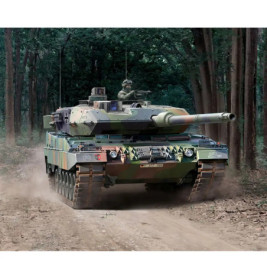 Ein getarnter Militärpanzer fährt auf einem Schotterweg durch einen dichten Wald.