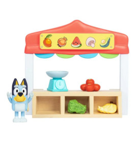 Bluey steht neben einem Spielzeug-Marktstand mit Obst, Gemüse und einer Waage auf der Theke.