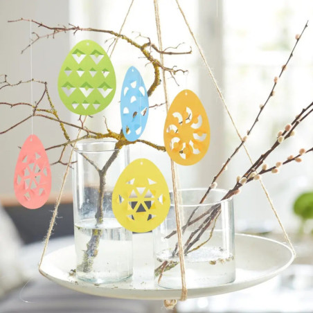 Bunte Papiergeier hängen an Zweigen in Glasvasen, die auf einem schwebenden weißen Teller stehen.