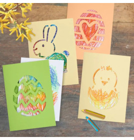 Vier bunte Ostkarten mit Wachsmalbildern von Ei, Hase, Herz und Küken liegen auf einem Holztisch.