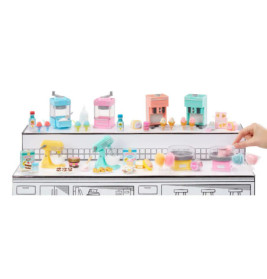 Miniatur-Küchengeräte und Süßigkeiten in Pastell auf weißer Theke, eine Hand hält Zuckerwatte.