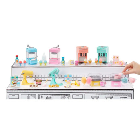 Miniatur-Küchengeräte und Süßigkeiten in Pastell auf weißer Theke, eine Hand hält Zuckerwatte.