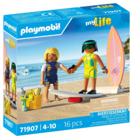 Zwei Playmobil-Figuren in Badekleidung stehen samt Surfbrett, Kamera und Zubehör auf Sand in einer Spielbox.