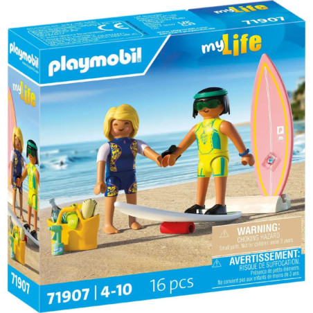 Zwei Playmobil-Figuren in Badekleidung stehen samt Surfbrett, Kamera und Zubehör auf Sand in einer Spielbox.
