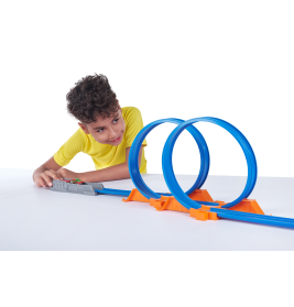 Ein Junge im gelben Shirt spielt mit einer blau-orangen Autorennbahn, die zwei Loopings hat.
