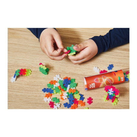 Kinderhände legen bunte Puzzle-Teile auf einen Holztisch, daneben steht ein roter Behälter.