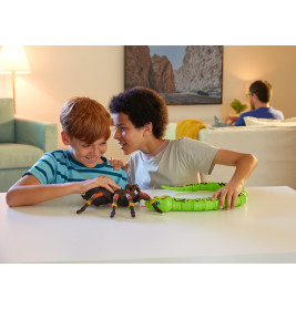 Zwei Jungen spielen lächelnd mit Spielzeug-Spinne und -Schlange an einem weißen Tisch im hellen Wohnzimmer.