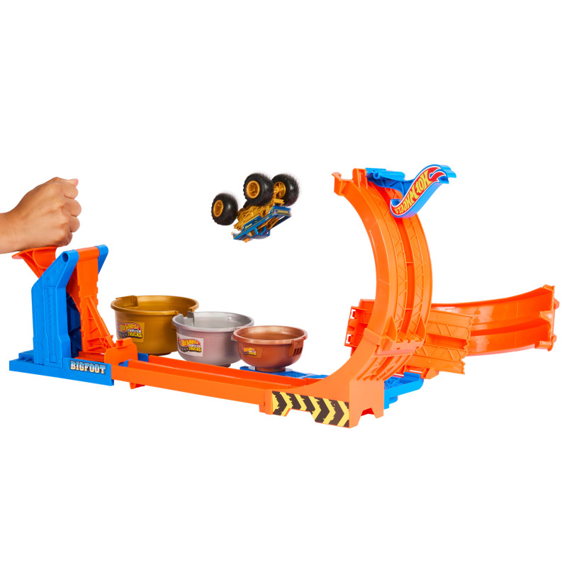 Eine Hand startet den Hot Wheels Monster Truck Loop & Flip Bigfoot auf einer orangenen Rampe zu drei Fässern.