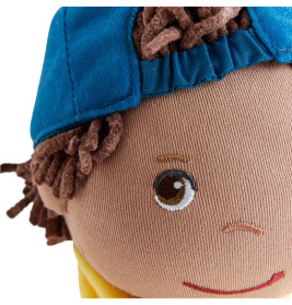 Nahaufnahme eines Stoffpuppengesichts mit braunen Wollhaaren, blauem Käppchen, gesticktem Lächeln und braunem Auge.