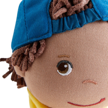 Nahaufnahme eines Stoffpuppengesichts mit braunen Wollhaaren, blauem Käppchen, gesticktem Lächeln und braunem Auge.