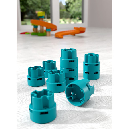 Acht türkisfarbene Bausteine liegen auf hellem Boden, im Hintergrund ist unscharf ein Spielzeugset zu sehen.