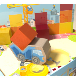 Ein blauer Spielzeugkipplaster transportiert einen roten Baustein, im Hintergrund Bauklötze und einen Kran.