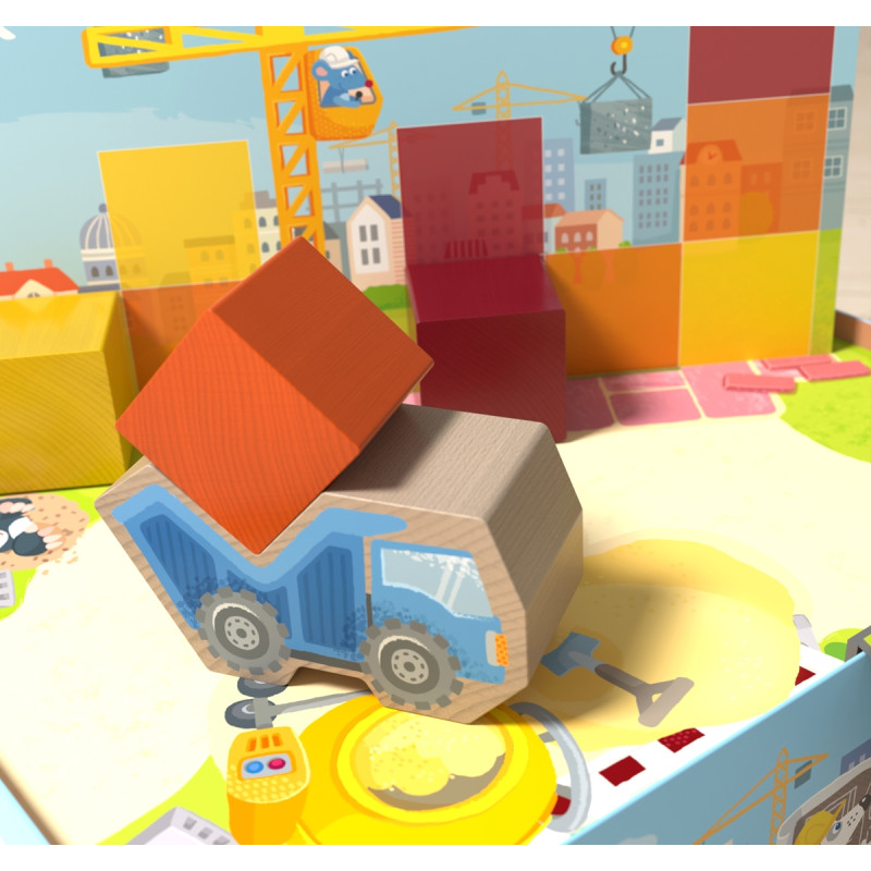 Ein blauer Spielzeugkipplaster transportiert einen roten Baustein, im Hintergrund Bauklötze und einen Kran.