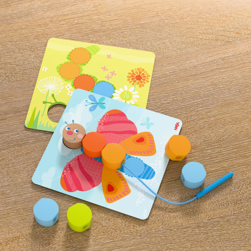 Steckspielzeug mit bunten Perlen sowie Schmetterlings- und Blumenkarten auf einem Holztisch.