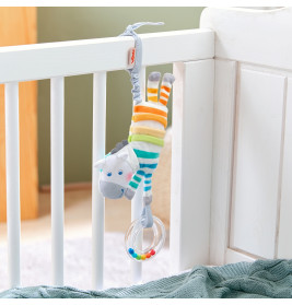 Plüschzebra mit bunten Streifen hängt am weißen Gitterbett und hält einen durchsichtigen Rasselring.