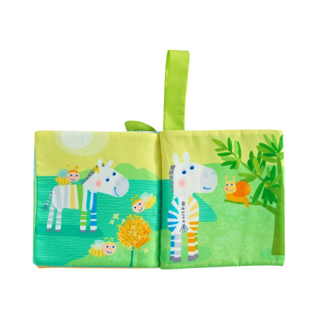 Stoff-Babybuch mit gezeichneten Zebras, Bienen und einer Schnecke in einer leuchtend grünen Landschaft.