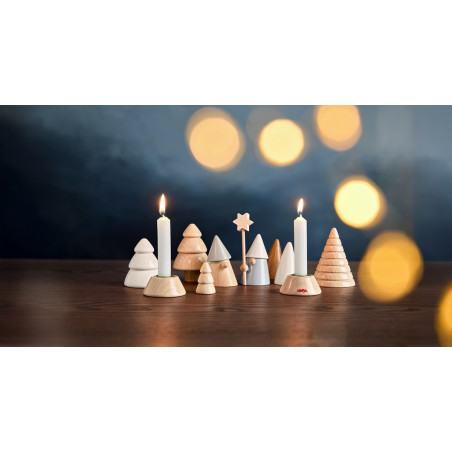 Holz- und Keramikbäume mit zwei brennenden Kerzen auf einem Tisch, unscharfe gelbe Lichter im Hintergrund.