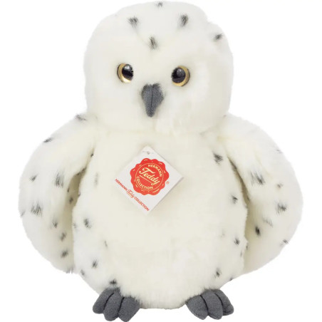 Weiße Schneeeule aus Plüsch mit schwarzen Flecken, gelben Augen und einem Schild auf der Brust.