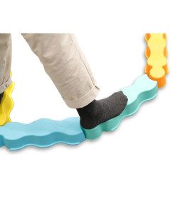 Eine Person mit grauen Socken läuft auf bunten, wellenförmigen Balancierbalken in Puzzleteilform.