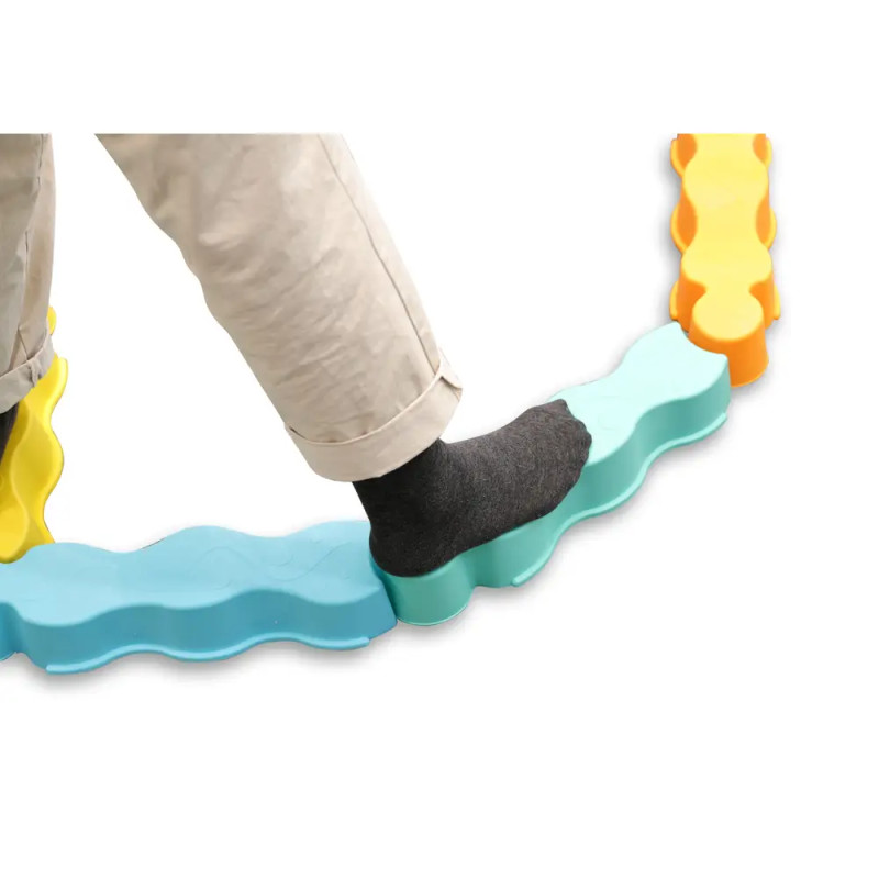 Eine Person mit grauen Socken läuft auf bunten, wellenförmigen Balancierbalken in Puzzleteilform.