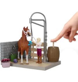 Eine Hand drückt ein Fass neben einem Spielzeugpferd und einem Mädchen im Stall-Spielset.