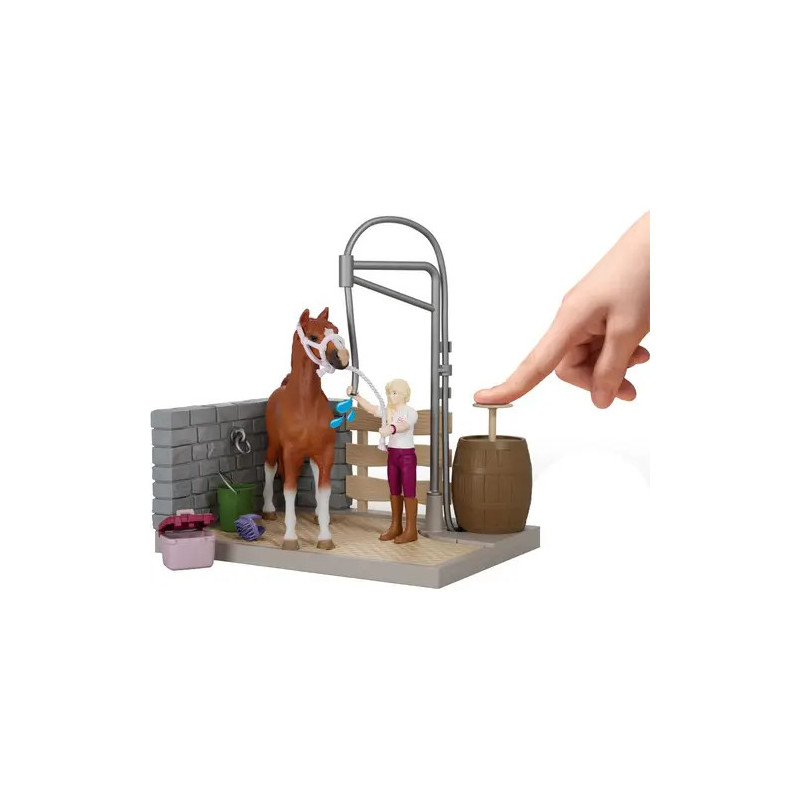 Eine Hand drückt ein Fass neben einem Spielzeugpferd und einem Mädchen im Stall-Spielset.