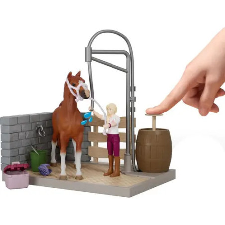 Eine Hand drückt ein Fass neben einem Spielzeugpferd und einem Mädchen im Stall-Spielset.