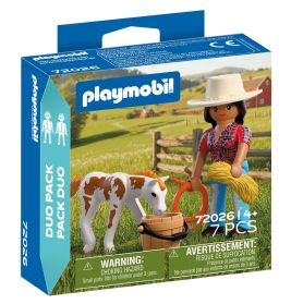 Playmobil-Set mit Frau im Hut, Kalb, Heuballen und weiteren Bauernhof-Zubehörteilen in ländlicher Umgebung.