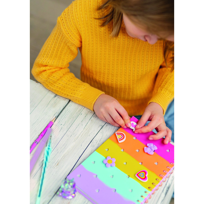 Kind im gelben Pullover verziert an einem weißen Holztisch ein buntes Notizbuch mit Aufklebern.