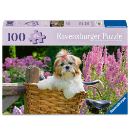 Ein flauschiger Hund mit Schleife sitzt im Fahrradkorb, umgeben von pinken Blumen; Puzzle mit 100 Teilen.
