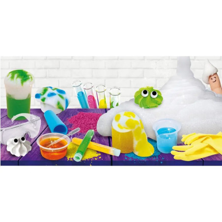 Bunte Laborausstattung mit Reagenzgläsern, Handschuhen, Schutzbrille, Schaum und Schleimfiguren auf einem lila Tisch.