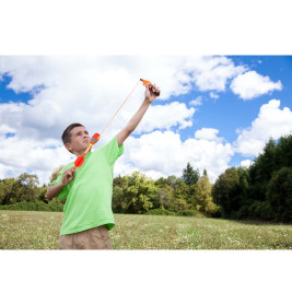 Ein Junge im grünen Shirt zielt mit Spielbogen und Pfeil auf einer Wiese unter blauem Himmel mit Wolken.