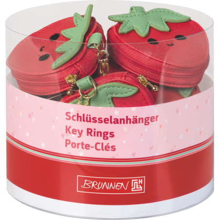 Runder Behälter mit roten Erdbeer-Schlüsselanhängern mit Gesicht, beschriftet auf Deutsch, Englisch und Französisch.