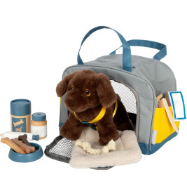 Plüschhund in einer Transportbox, umgeben von Spielzeugfutter, Napf, Leine und weiterem Zubehör.