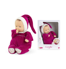 Eine Babypuppe im lila Outfit mit passender Mütze sitzt neben ihrer Verpackungsschachtel.