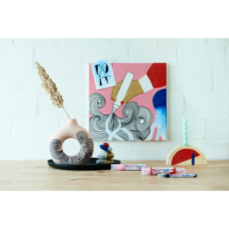 Kunstmaterialien und eine Vase stehen vor einem bunten Gemälde mit der Aufschrift "DO IT" an der Wand.