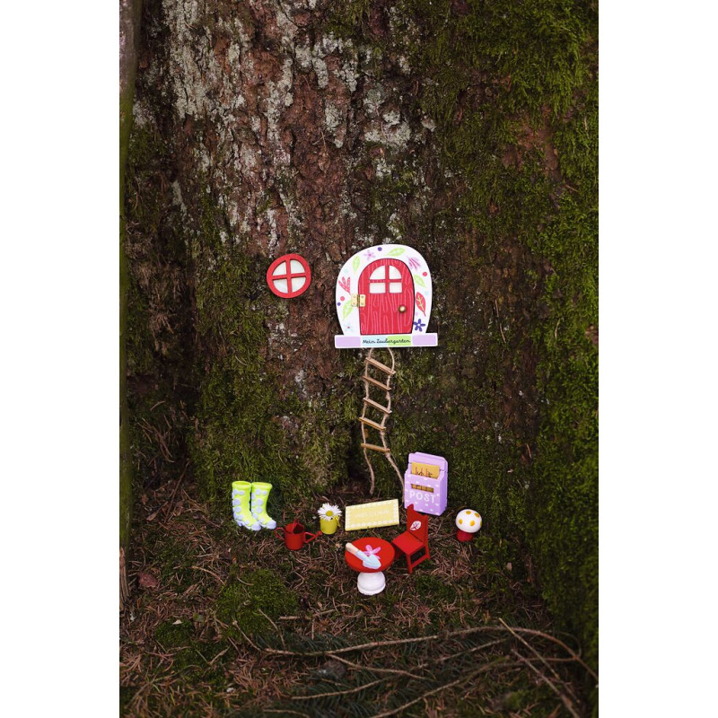 Kleine Feentür mit Leiter, Möbeln und Dekoration am Fuß eines moosbedeckten Baumstamms.