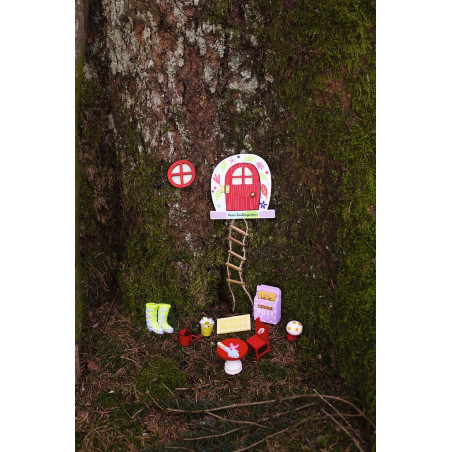 Kleine Feentür mit Leiter, Möbeln und Dekoration am Fuß eines moosbedeckten Baumstamms.