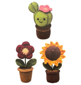 Drei gehäkelte Topfpflanzen: Kaktus mit rosa Blüte, rote Blume und Sonnenblume, alle mit lächelnden Gesichtern.