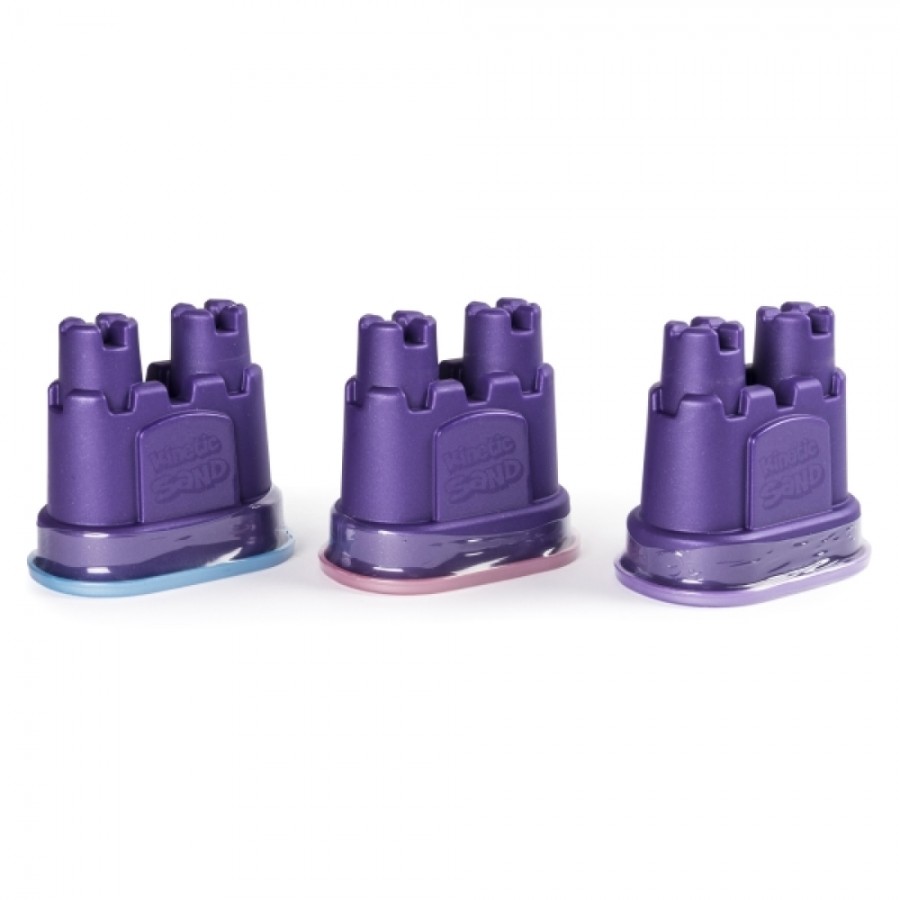 Drei kleine lila Sandburgformen mit verschiedenfarbigen Böden stehen nebeneinander.