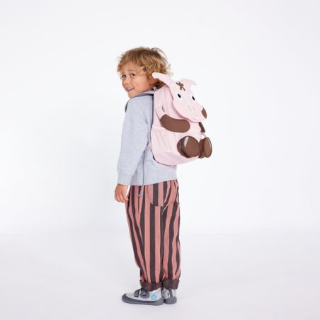 Ein Kind mit grauem Hoodie, gestreifter Hose und pinkem Tier-Rucksack lächelt in die Kamera.